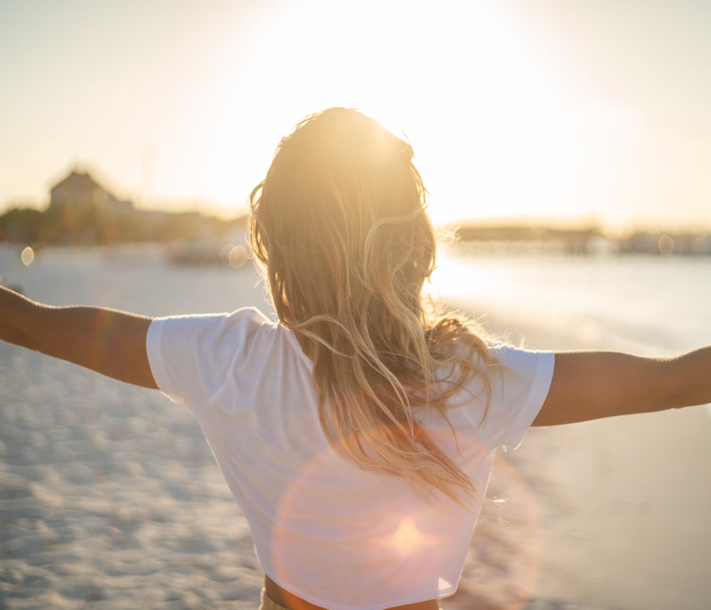 A woman at the beach with her arms outstretched looking towards the sun.