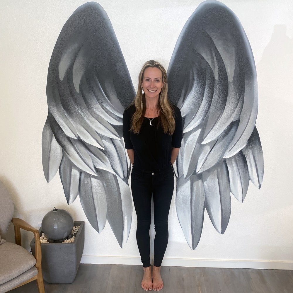 Refuge Acupuncture Founder Tracey Abbott standing in front of wing painting in upstairs apothecary area