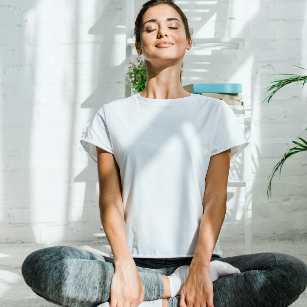 A smiling woman with her legs crossed in a yoga pose