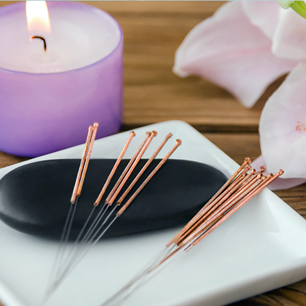 A lit candle is placed next to seven acupuncture pins