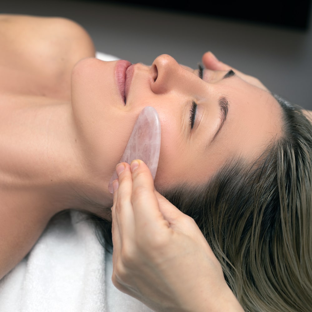 A flat stone being scraped against a patient's face during a Gua Sha facial.