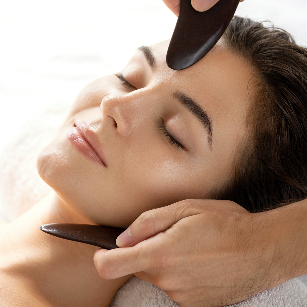 Two flat Gua Sha implements being pressed against the face of a patient during treatment