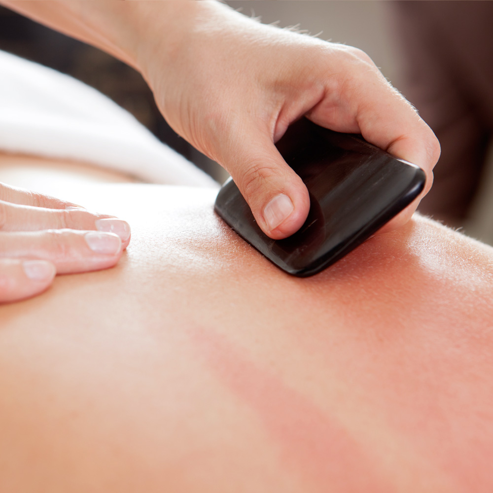 A Refuge practitioner conducting a Gua Sha massage, using a flat stone scraper, at the Denver Refuge office.