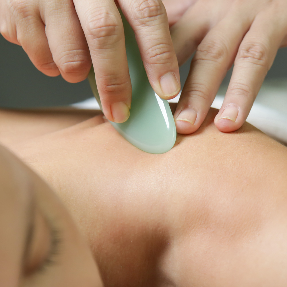 A Refuge practitioner using a jade Gua Sha scraper to massage a patient.