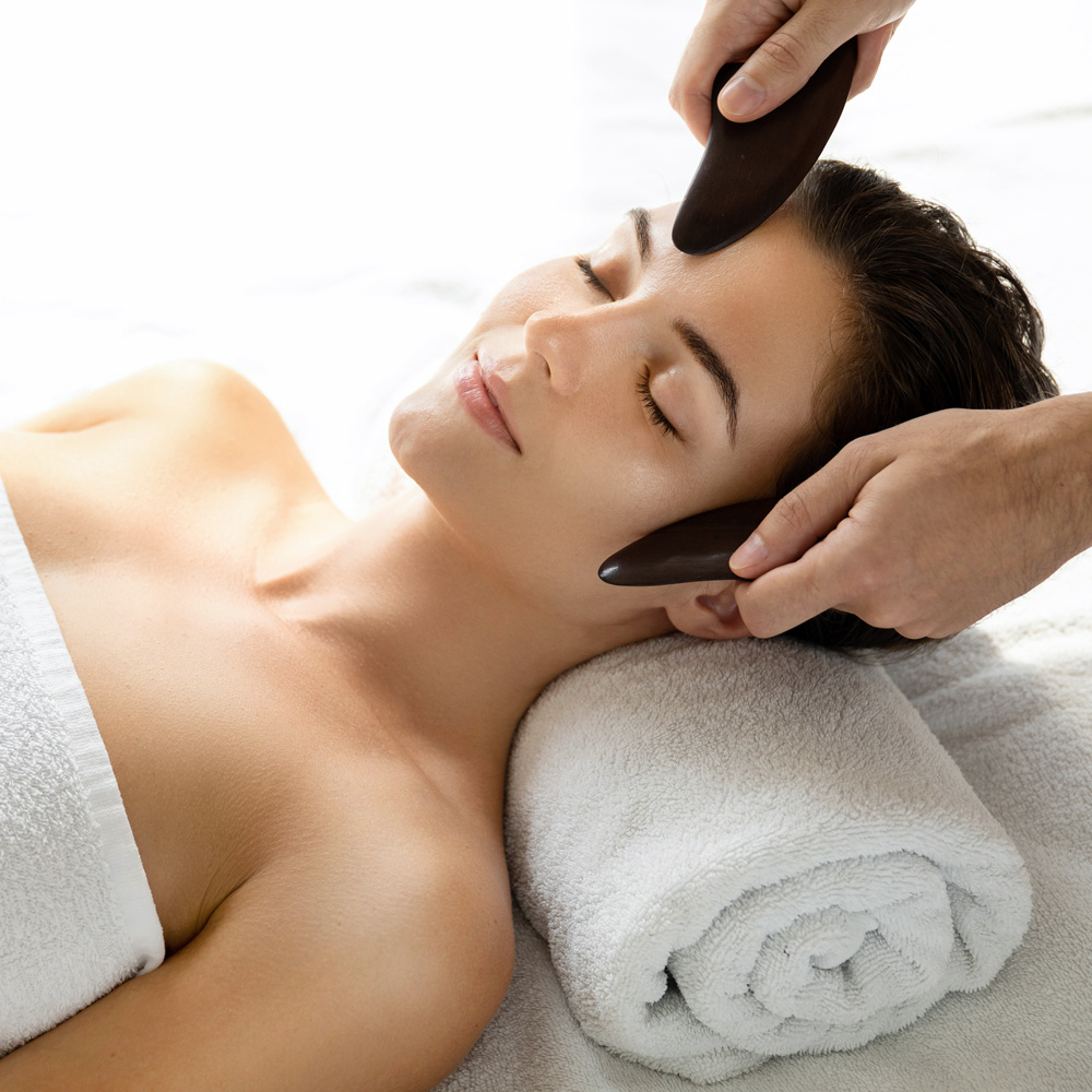 Two flat Gua Sha implements being pressed against the face of a patient during treatment.