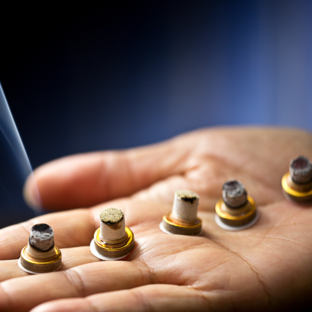 A close up of a hand on which lit moxibustion bundles are placed.