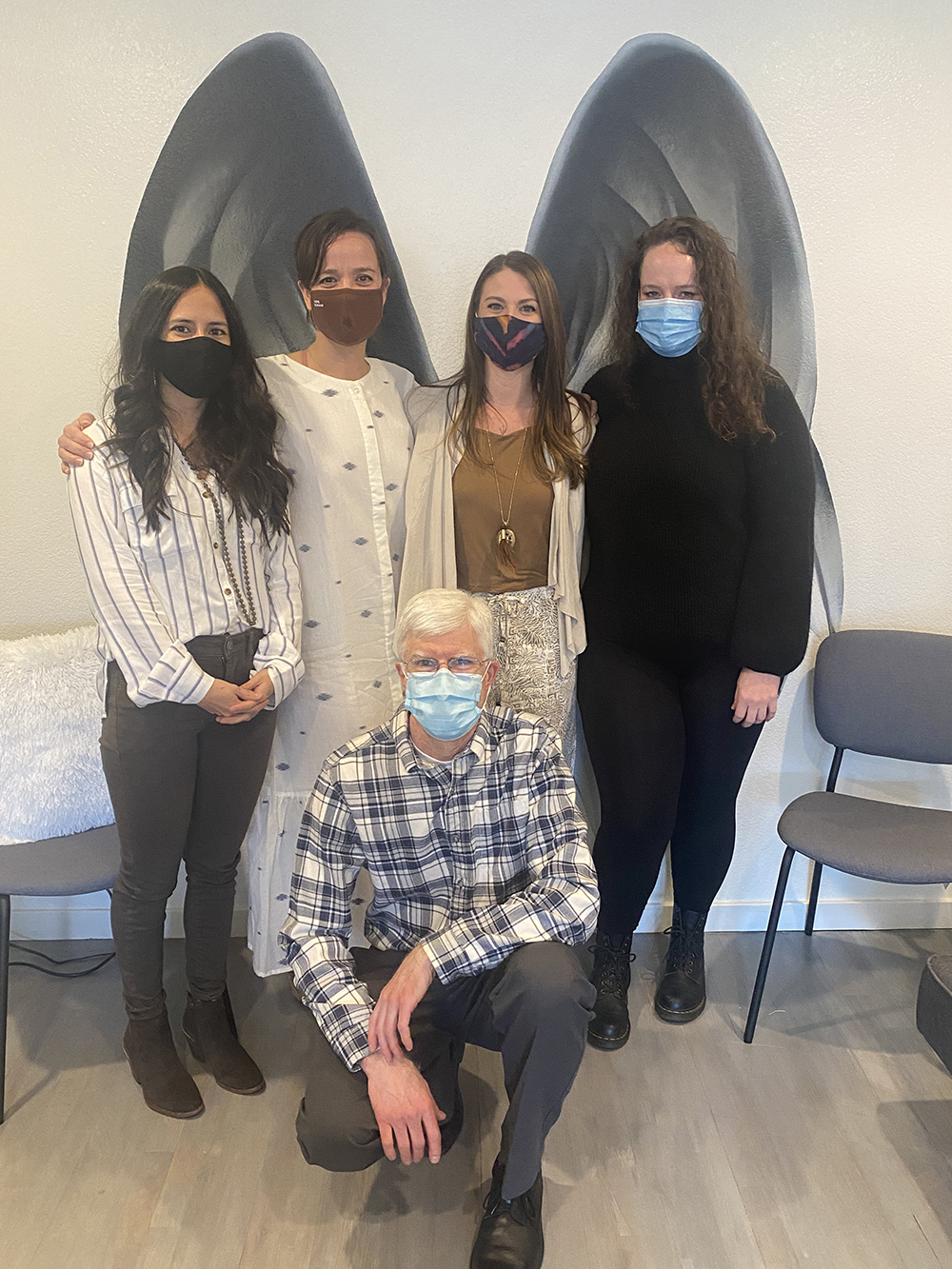 Patient specialists, Lisa Rundall, Elena Beltran, and Kristin Black, standing with Michael Harman and Dr. Caitlin R. Dilli standing in front of a wall on which angel wings are depicted.